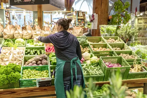 Frau räumt im Supermarkt Gemüse ein